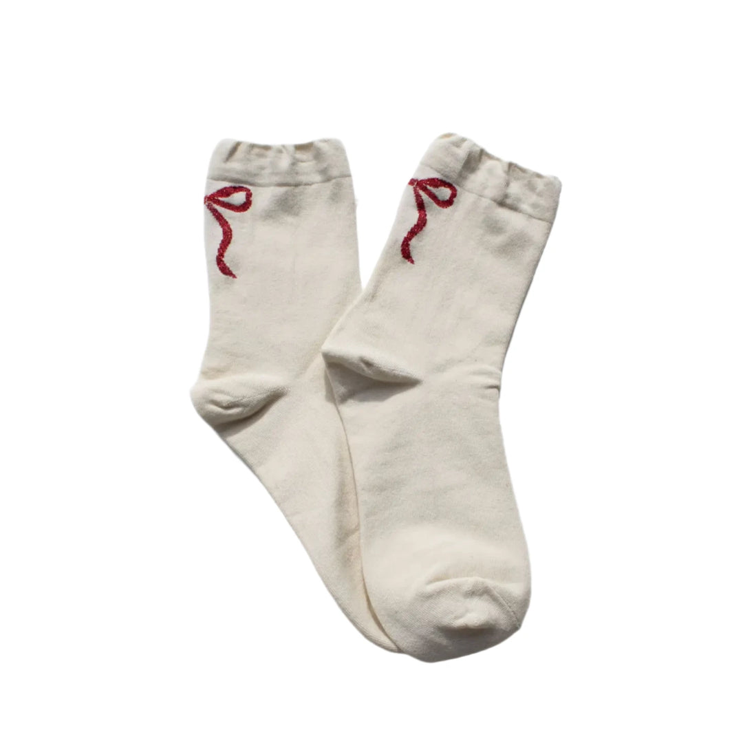 A pair of cream socks with a glittery ribbon detail near the top, laid flat on a white textured background, showcasing their elegant and minimalist design.