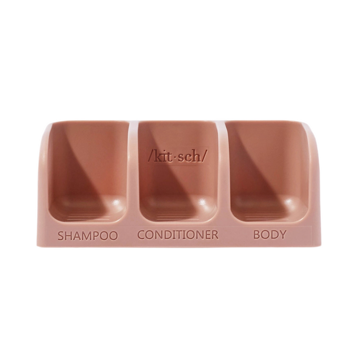 front view of a light pink soap dish that has three compartments with the words shampoo, conditioner and body at each compartment.