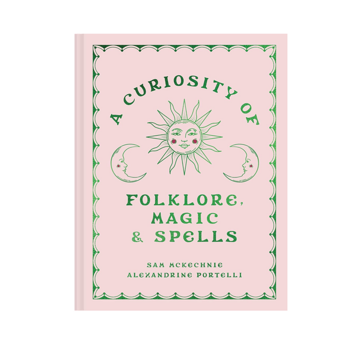 Book cover of 'A Curiosity of Folklore, Magic & Spells' features a light pink background with green text and illustrations of a sun and two crescent moons with faces. 