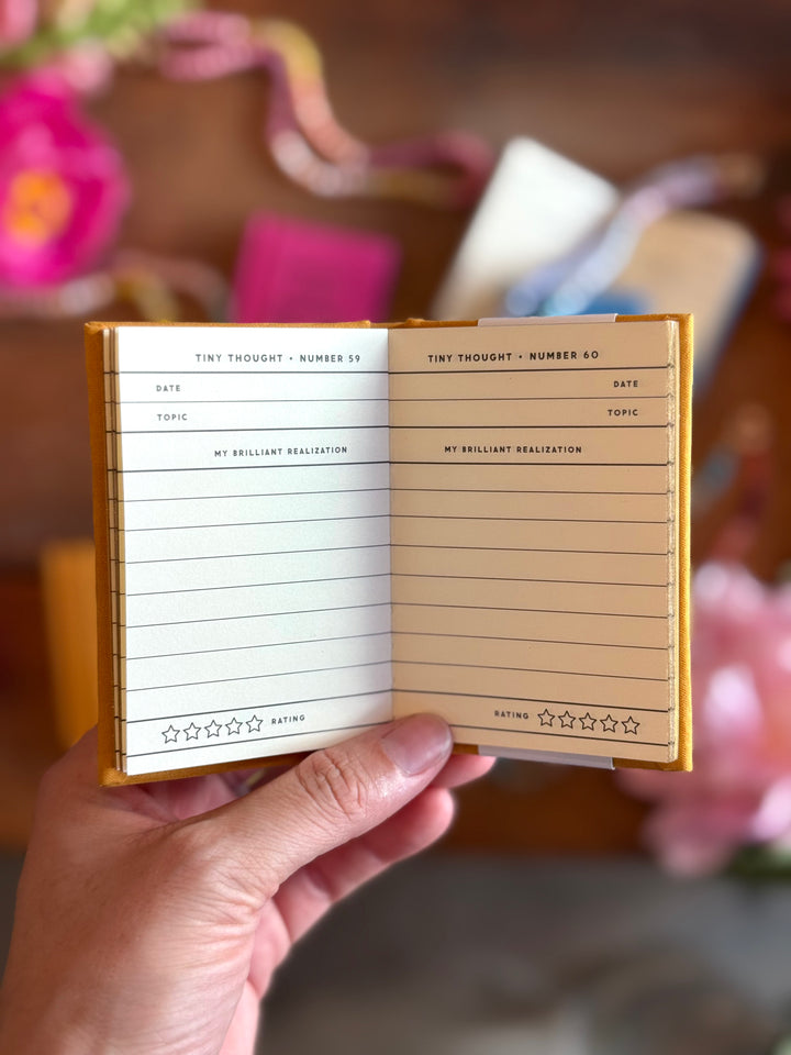 Hand holding a small notebook with lined pages and floral background