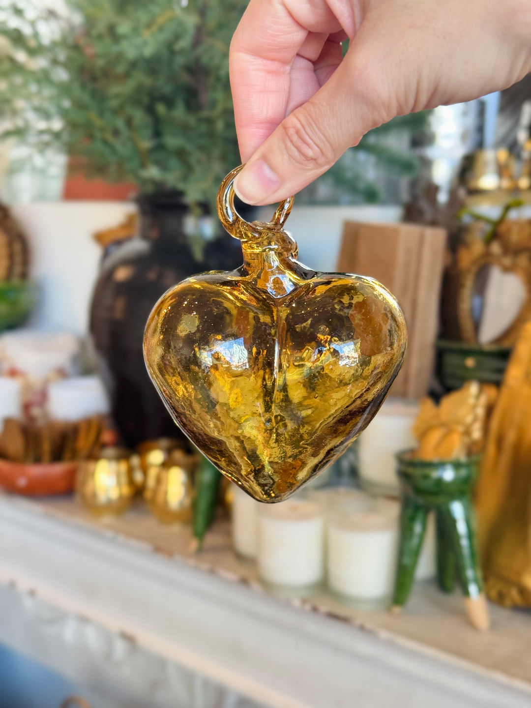 Hand holding a heart-shaped amber-colored ornament with a blurred indoor setting in the background.