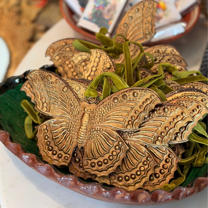 antique gold butterfly ex voto embossed with dotted and ridged detail across its scalloped wings featuring a green velvet loop.