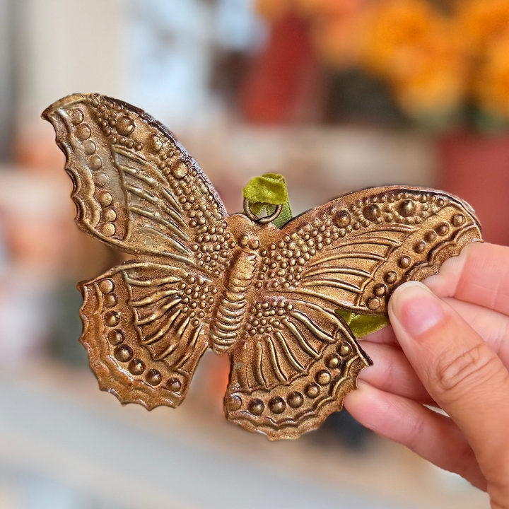 antique gold butterfly ex voto embossed with dotted and ridged detail across its scalloped wings featuring a green velvet loop.