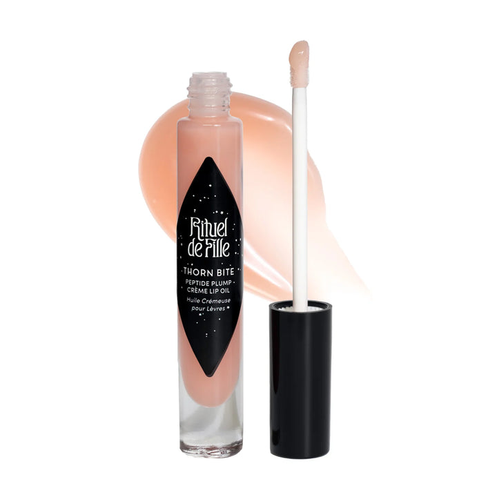 clear tube of light peach shaded lip oil with a black branded label and lip with a swatch of the lip oil behind it. Brand: Rituel De Fille