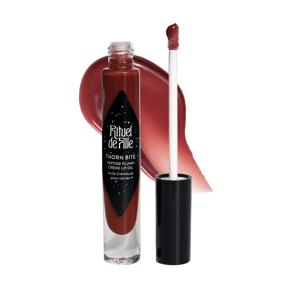 clear tube of dark rose shaded lip oil with a black branded label and lip with a swatch of the lip oil behind it. Brand: Rituel De Fille