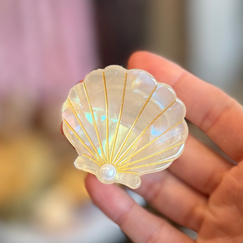 White Iridescent seashell-shaped hair claw clip with gold detailing and a pearl accent.