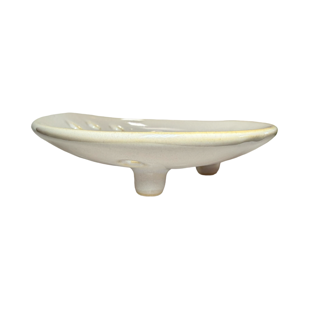 side view of a round ceramic footed soap dish with perforated drainage holes, shown in white.