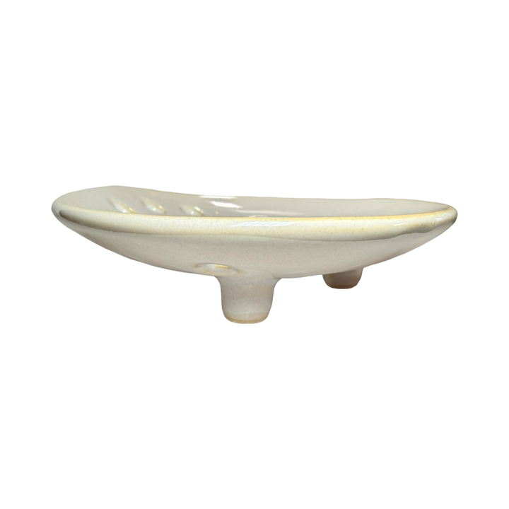 side view of a round ceramic footed soap dish with perforated drainage holes, shown in white.