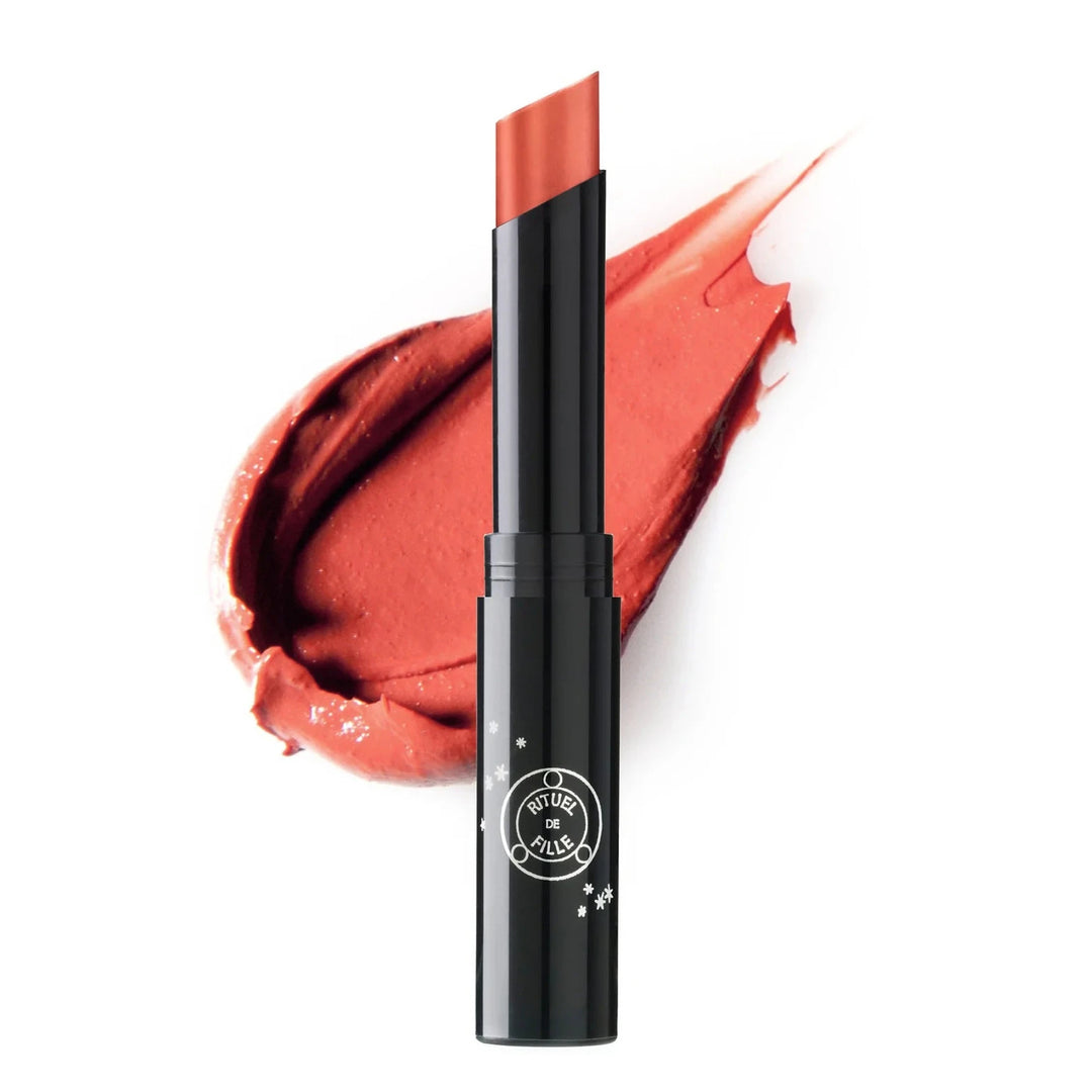 black branded tube of red orange shade lipstick with a color swatch behind it. Brand: Rituel De Fille