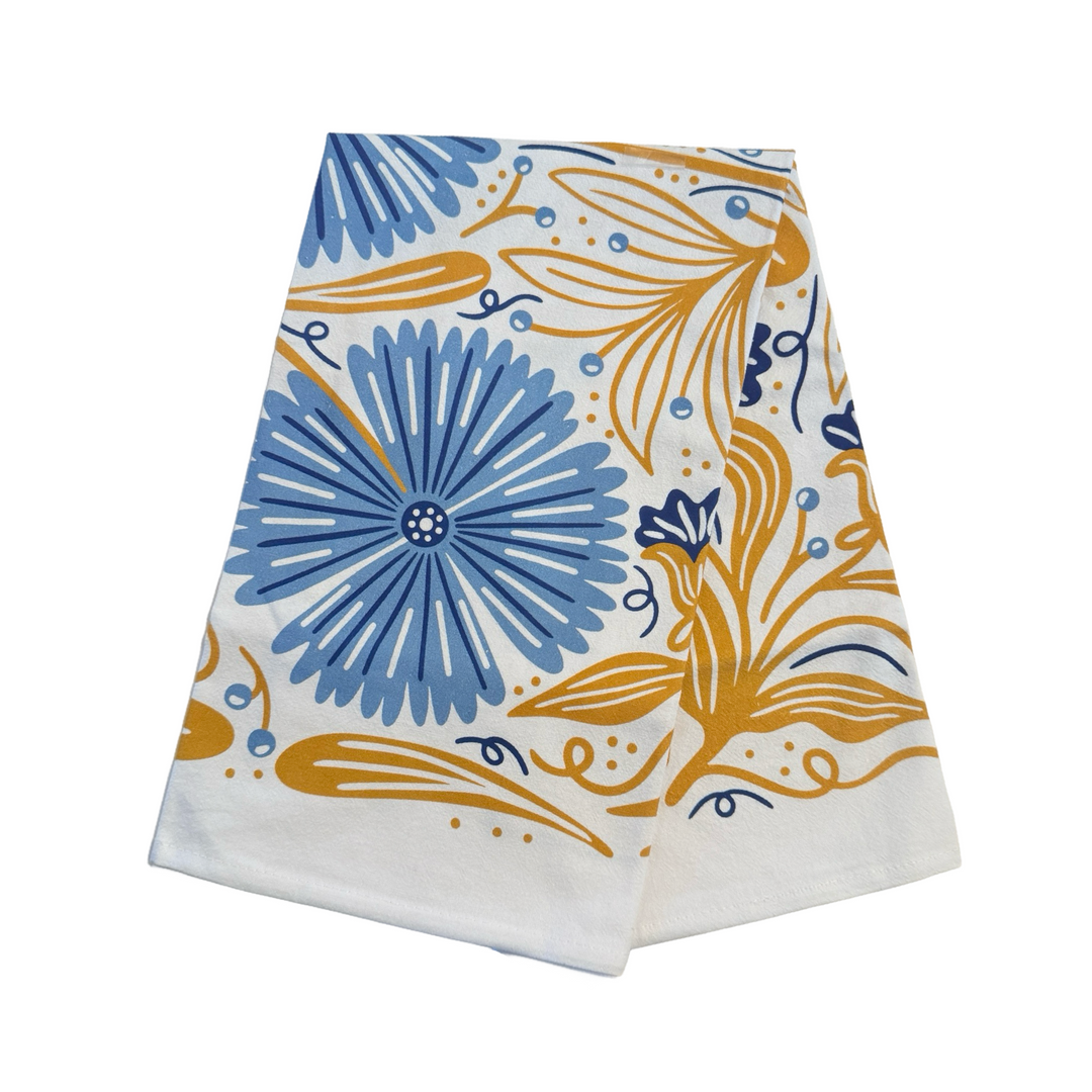 White Cotton tea towel held open, displaying a symmetrical floral pattern with large blue flowers, golden leaves, and blue caterpillars folded in quarters.