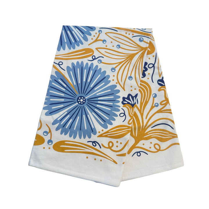 White Cotton tea towel held open, displaying a symmetrical floral pattern with large blue flowers, golden leaves, and blue caterpillars folded in quarters.