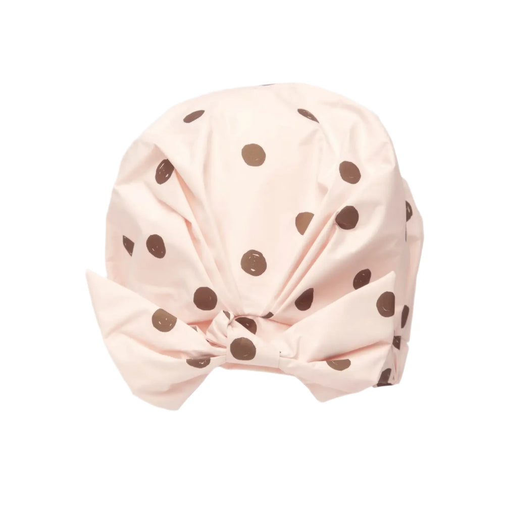 A blush pink shower cap with brown polka dots featuring a stylish bow detail at the front. 