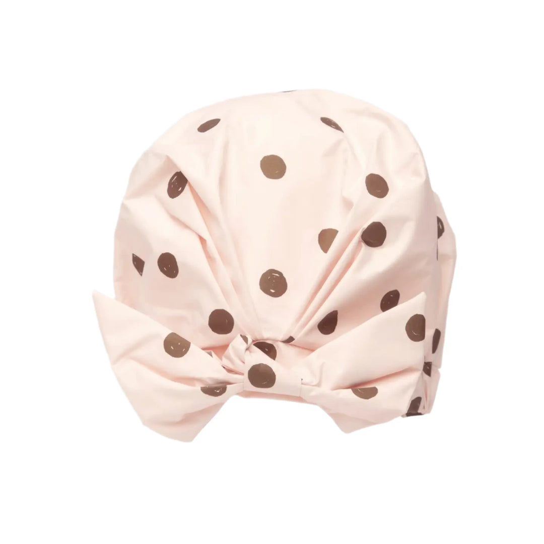 A blush pink shower cap with brown polka dots featuring a stylish bow detail at the front. 