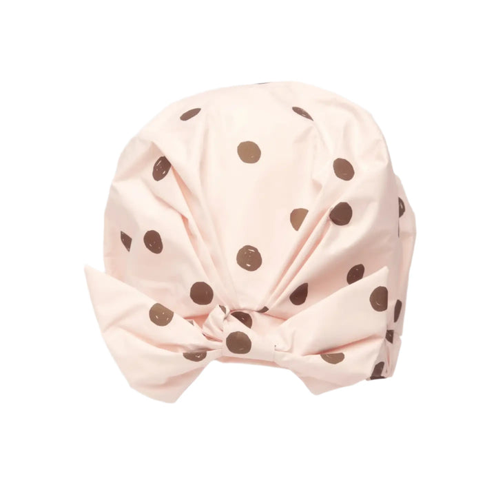 A blush pink shower cap with brown polka dots featuring a stylish bow detail at the front. 