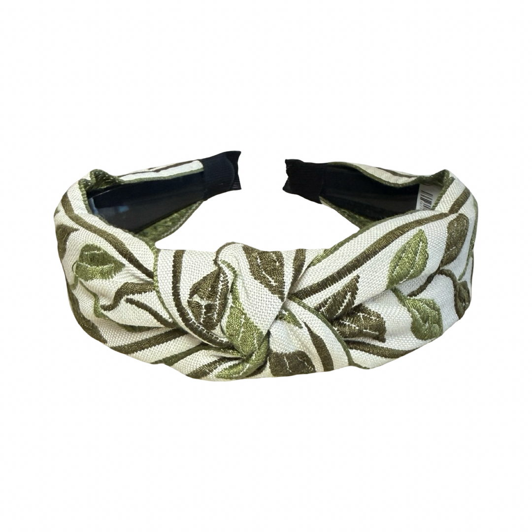 Top view of A knotted fabric headband with an olive green embroidered leaf pattern on a cream background.