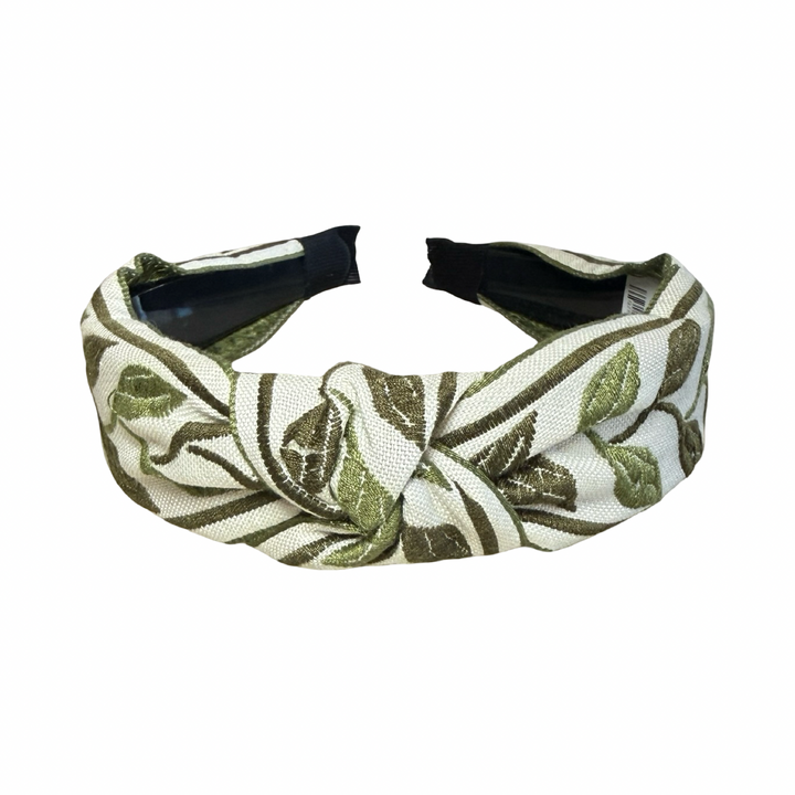 Top view of A knotted fabric headband with an olive green embroidered leaf pattern on a cream background.