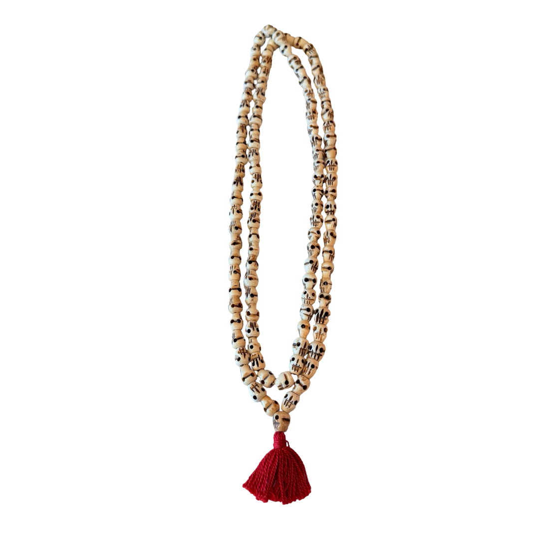 Long mala necklace made of carved bone skull beads in ivory tones, strung on a cord with a knotted tassel.