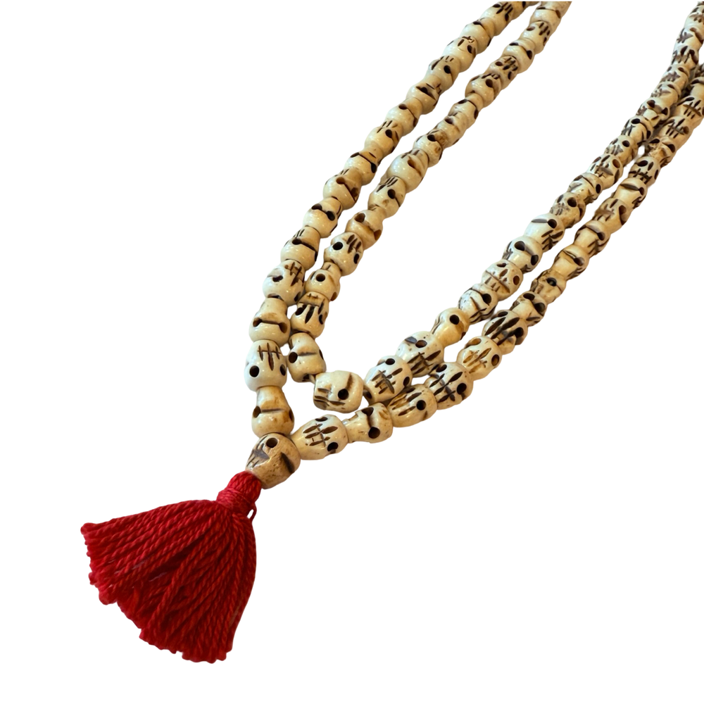 Close up of a Long mala necklace made of carved bone skull beads in ivory tones, strung on a cord with a knotted tassel.