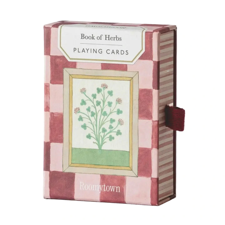 Book of Herbs Playing Card Deck box by Roomytown, featuring a rosy pink and red checkerboard pattern, a botanical herb illustration at the center, and a small burgundy ribbon pull tab on the side.
