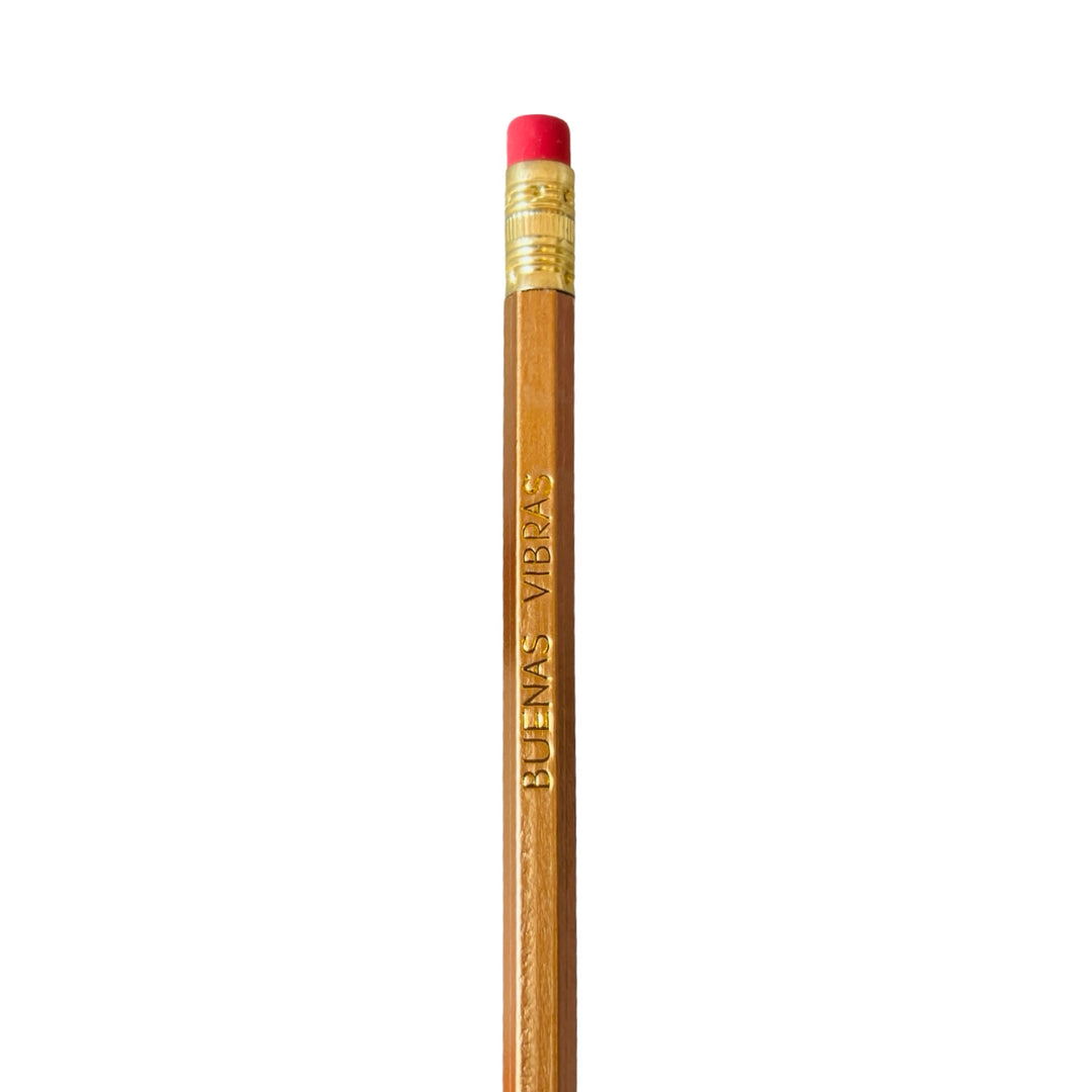 A wooden pencil with 'BUENAS VIBRAS' printed in gold lettering on the side, topped with a red eraser.