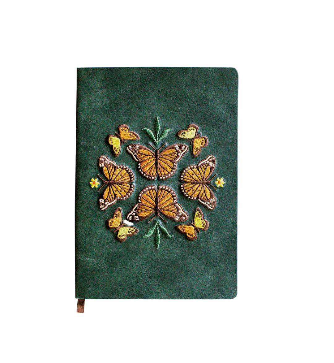 Dark green journal with an embroidered motif of orange butterflies circling a small plant and tiny yellow flowers, finished with a ribbon bookmark at the bottom.