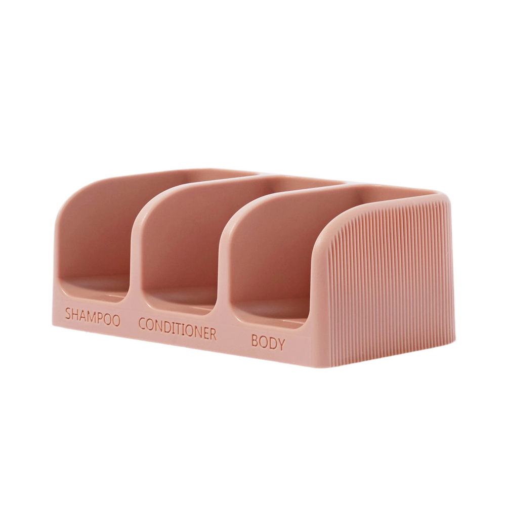 side view of a light pink soap dish that has three compartments with the words shampoo, conditioner and body at each compartment.