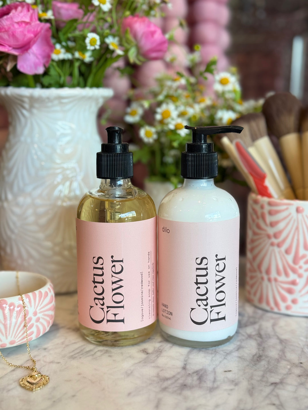 Two 'Cactus Flower' bottles on a marble surface with flowers and decorative items in the background.