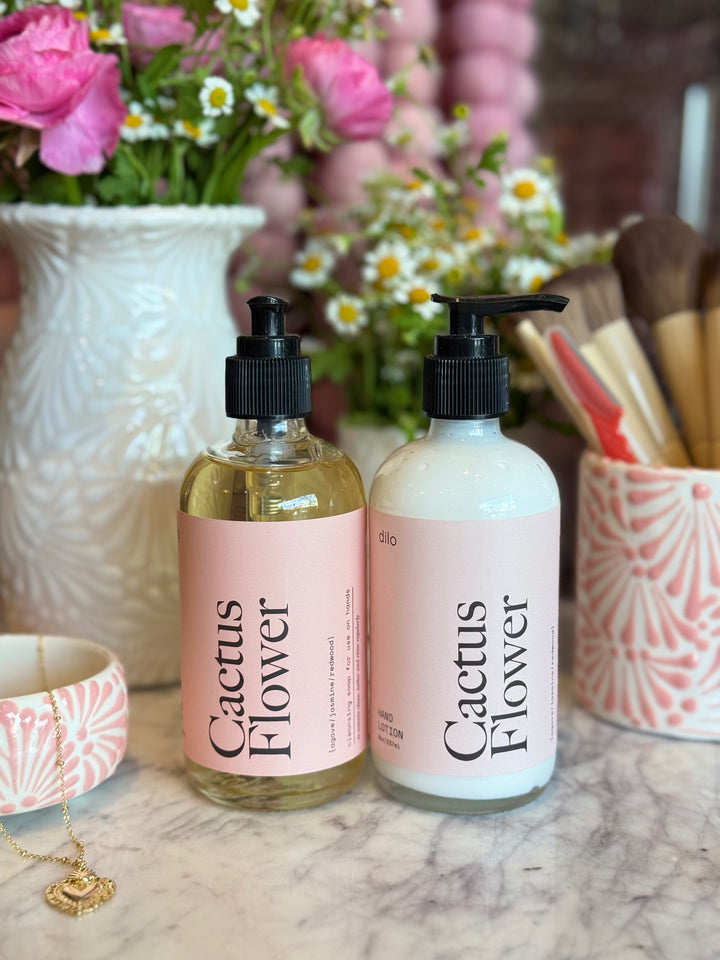 Two 'Cactus Flower' bottles on a marble surface with flowers and decorative items in the background.