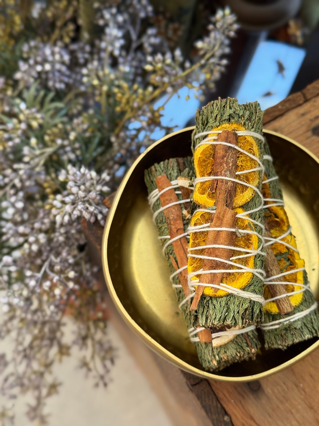 Three smudge sticks in a gold dish with a blurred natural background
