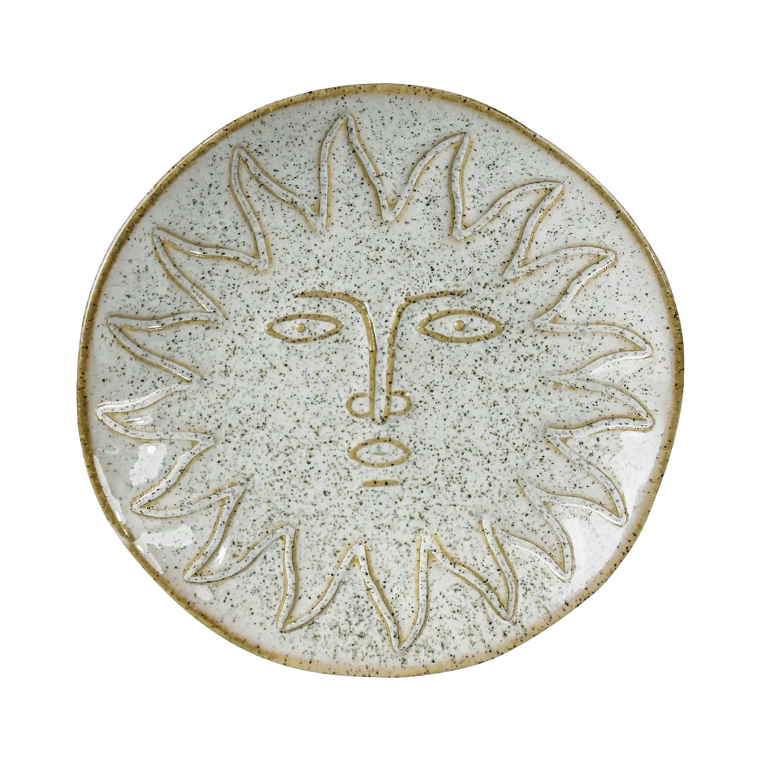 Round ceramic dish with a speckled white glaze and an etched sun face design with radiating rays and stylized facial features.