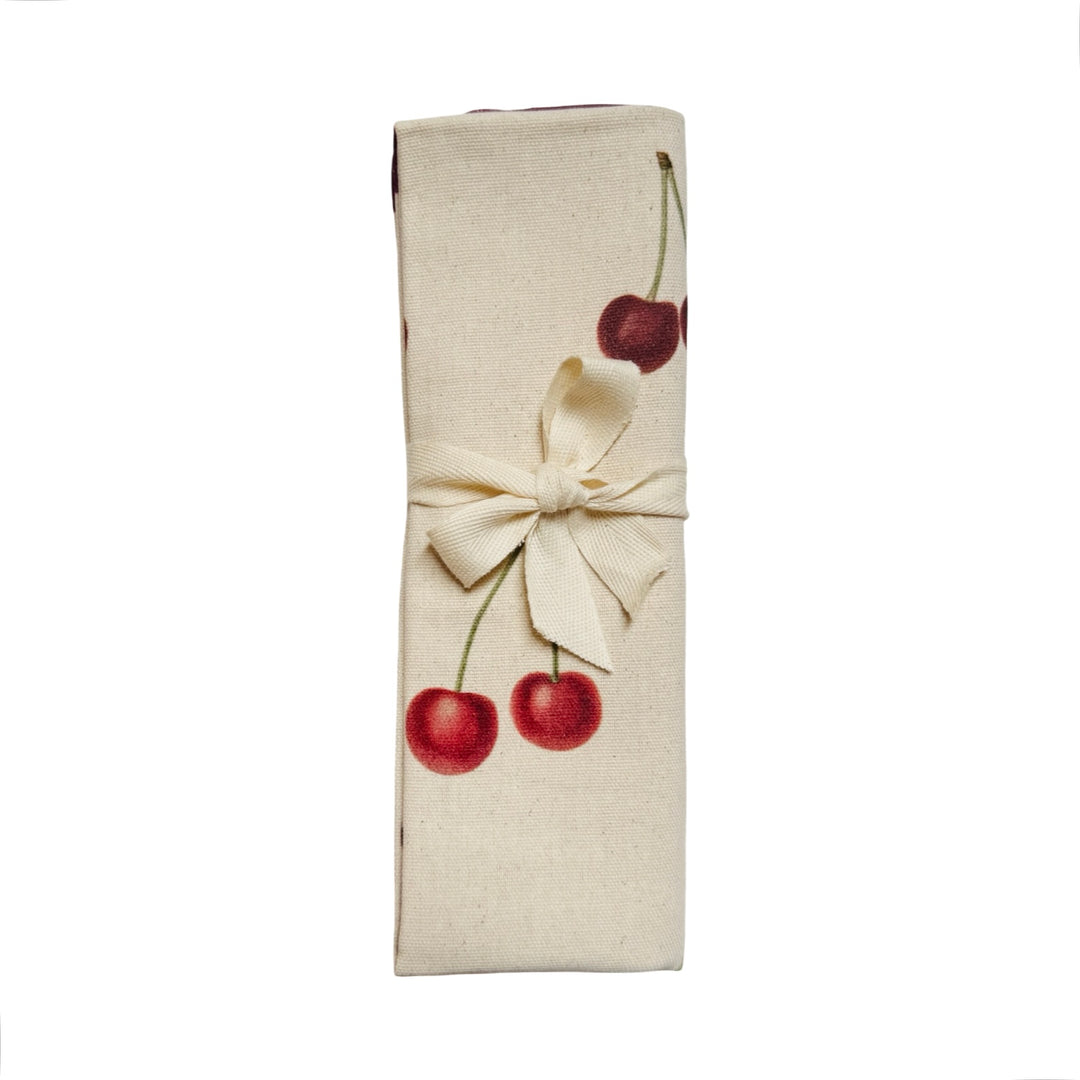 Tea towel featuring a repeating pattern of illustrated cherries folded in half tied with a ribbon.