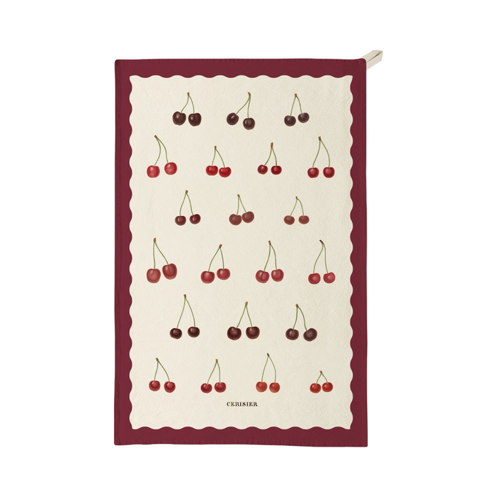 Tea towel featuring a repeating pattern of illustrated cherries with a decorative border and the word “Ceriser” printed near the bottom.