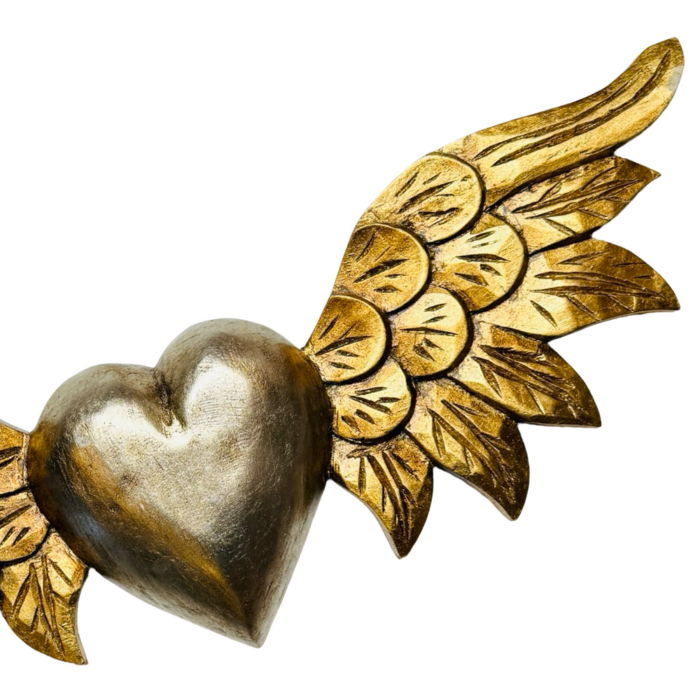 close up view of Hand-carved wooden Sacred Heart with Wings wall décor featuring a silver-painted heart center and gold-toned angel wings with detailed feather carvings, handmade in San Miguel de Allende, Mexico.