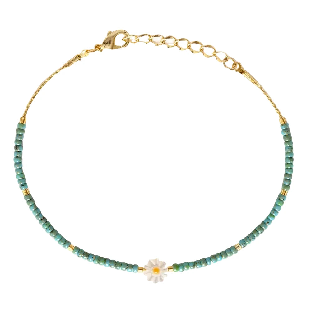 A delicate beaded bracelet featuring small turquoise Japanese seed beads and gold tube accent beads with a white daisy flower centerpiece, finished with a gold lobster clasp and extender chain,