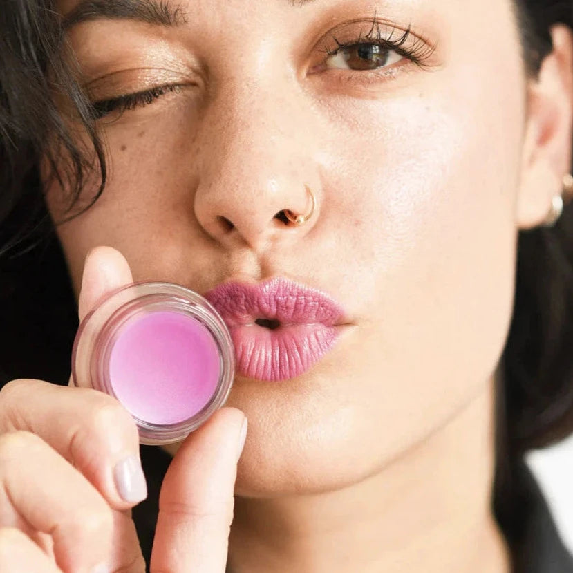 a woman holding a pink color pot to her lips while pursing her lips and winking