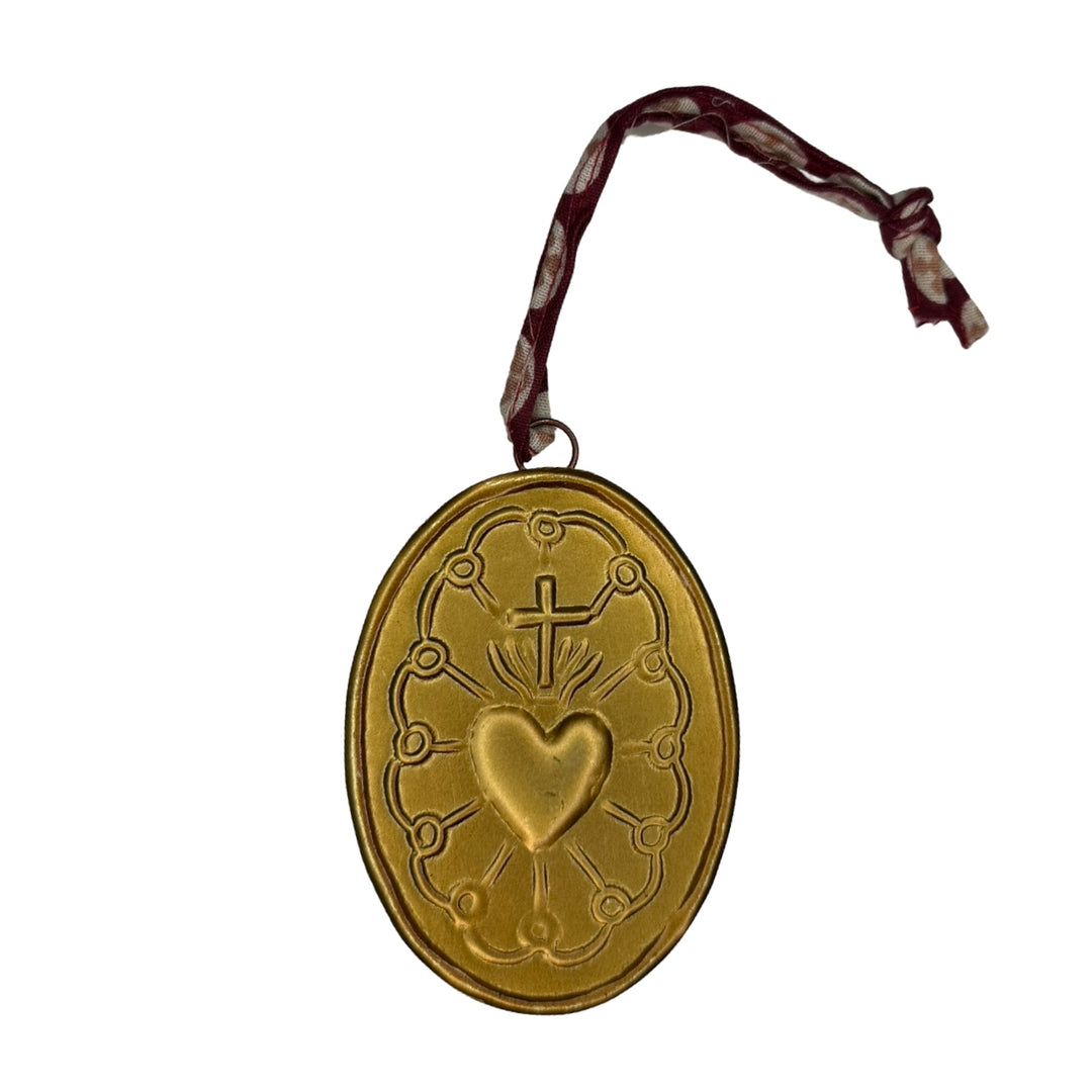 Gold oval medallion features a sacred heart and cross design and a brown ribbon hanger.