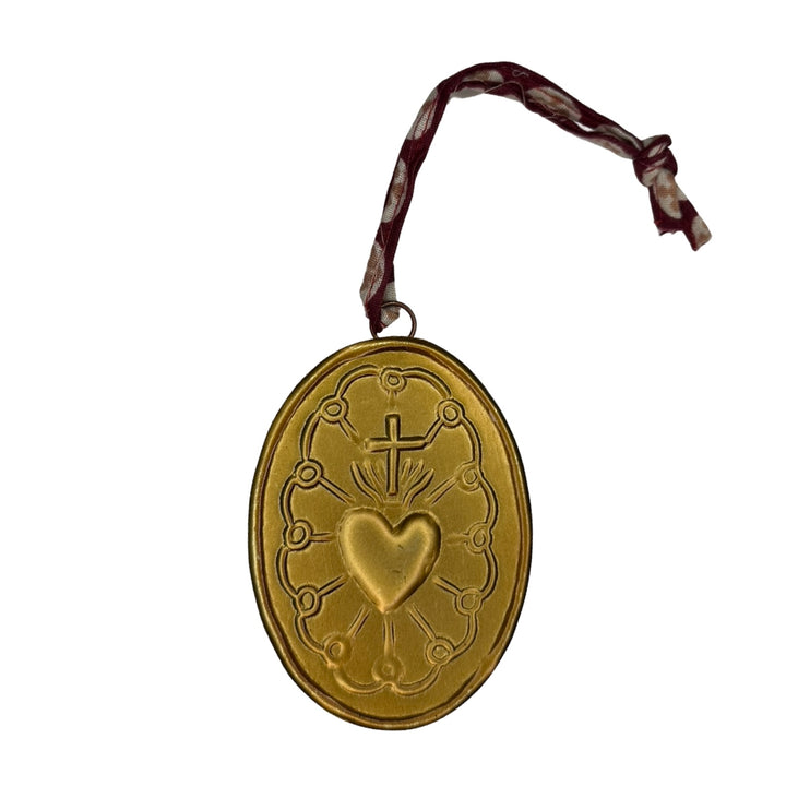 Gold oval medallion features a sacred heart and cross design and a brown ribbon hanger.