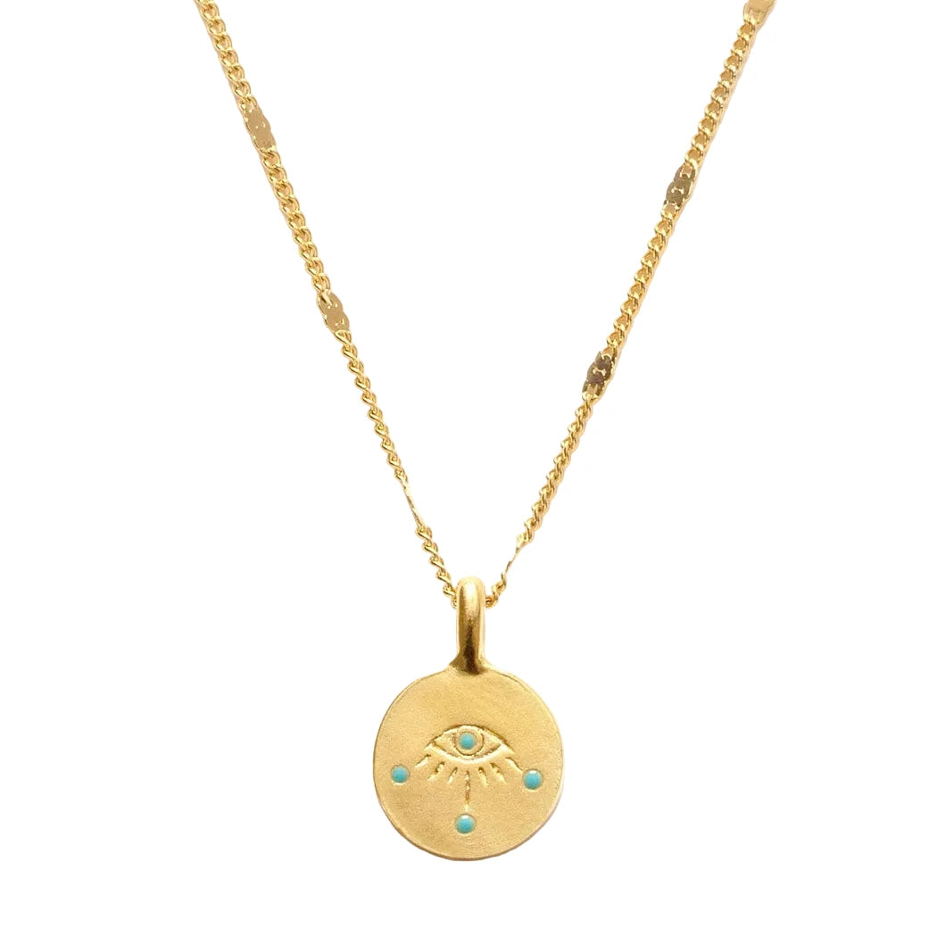 A close-up of a small round gold coin pendant featuring an engraved evil eye with turquoise enamel dot accents, hung on a delicate mixed gold chain with flat bar and curb link details.