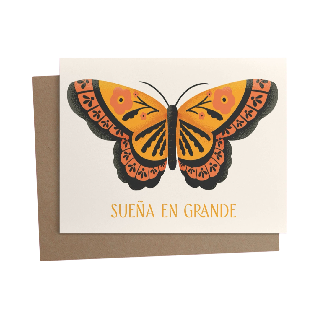 brown envelope behind a cream card with an illustration of a monarch butterfly and theh phrase Suena En Grande in orange lettering