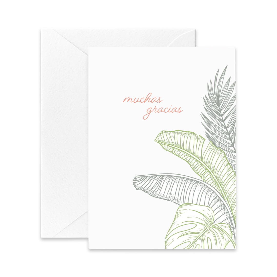 white card with an illustration of green tropical plants and the phrase muchas gracias in light pink lettering