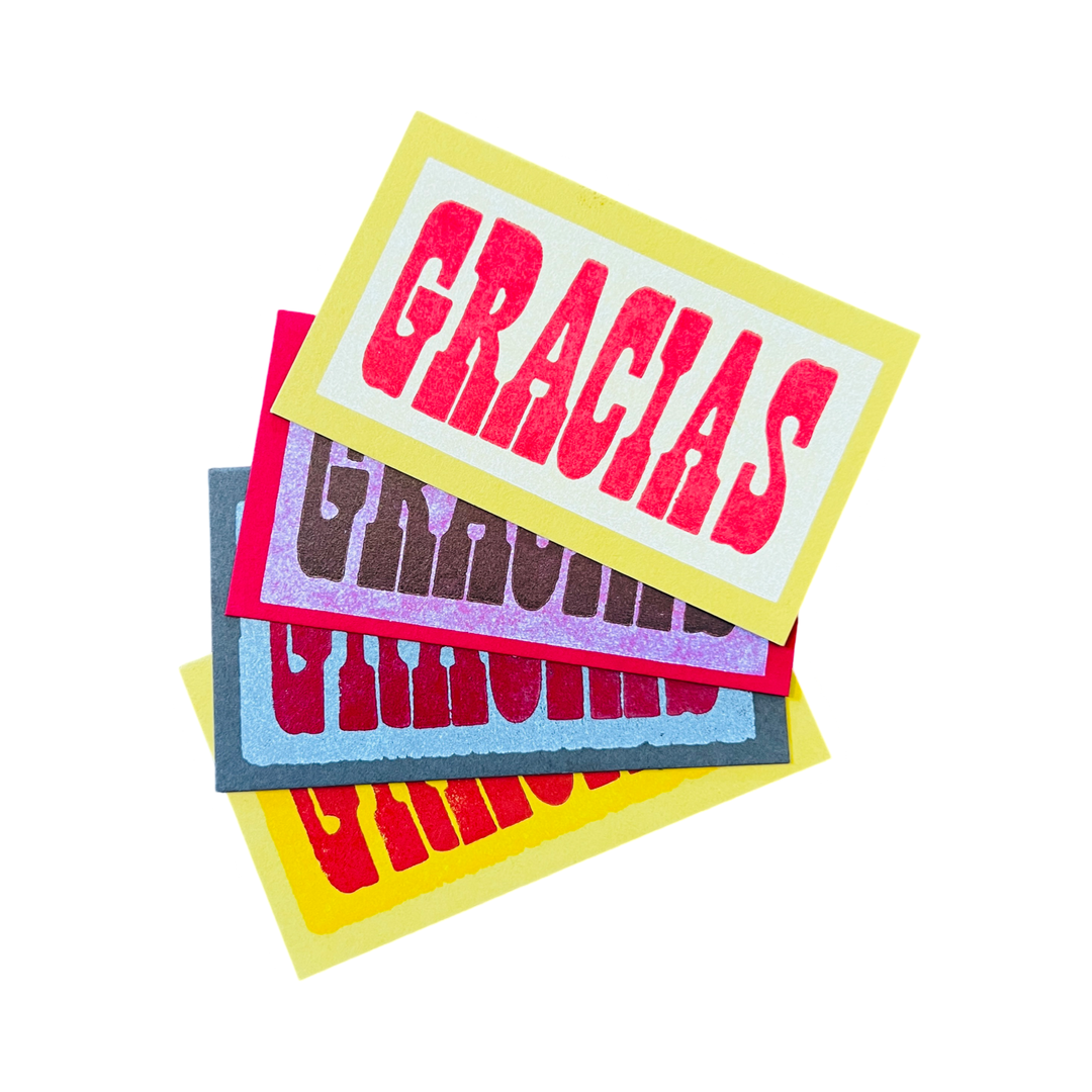 A stack of colorful mini cards with the word "GRACIAS" printed in bold, vintage-style typography. The cards come in a mix of red, blue, green, and yellow hues, creating a vibrant and cheerful expression of gratitude.