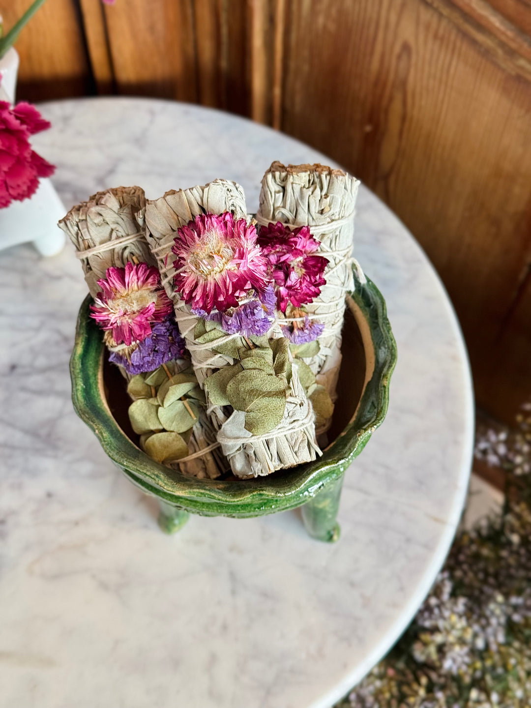Three smudge sticks with flowers in a green ceramic holder on a marble surface.
