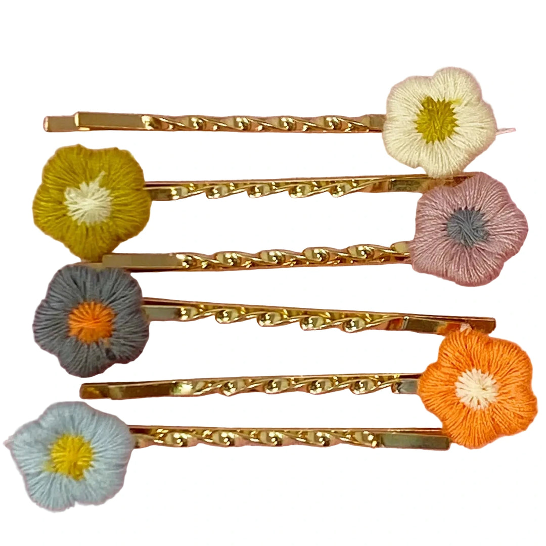Set of six gold bobby pins, each topped with a colorful embroidered flower in shades of cream, mustard, pink, gray, orange, and light blue.