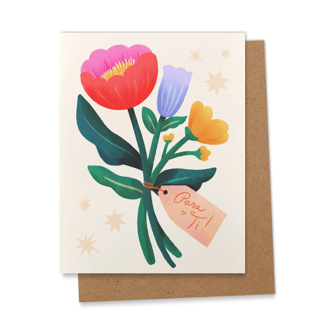 A greeting card featuring a bold illustrated floral bouquet of red, pink, lavender, and yellow flowers with dark green stems and leaves, tied together with a gift tag reading 'Para Ti!' surrounded by star motifs on a cream background, displayed propped against a kraft brown envelope.
