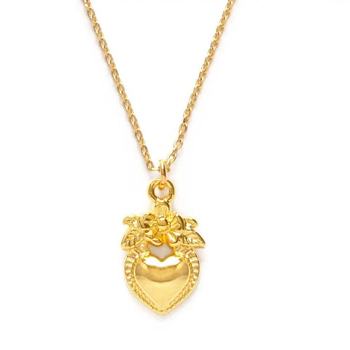 Close-up of a small gold-tone folk heart pendant with a floral crown detail on a fine chain.