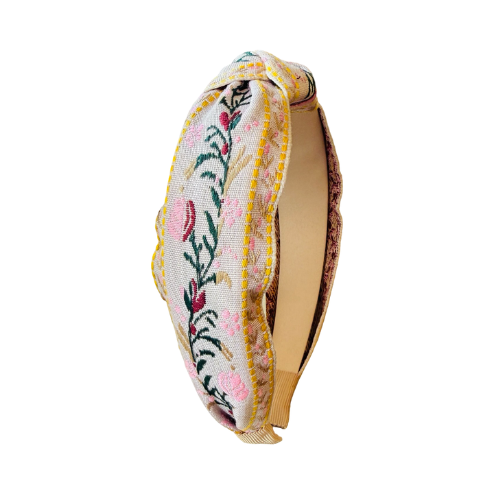 cream headband with a flower design in pink,maroon and yellow with some green foliage.