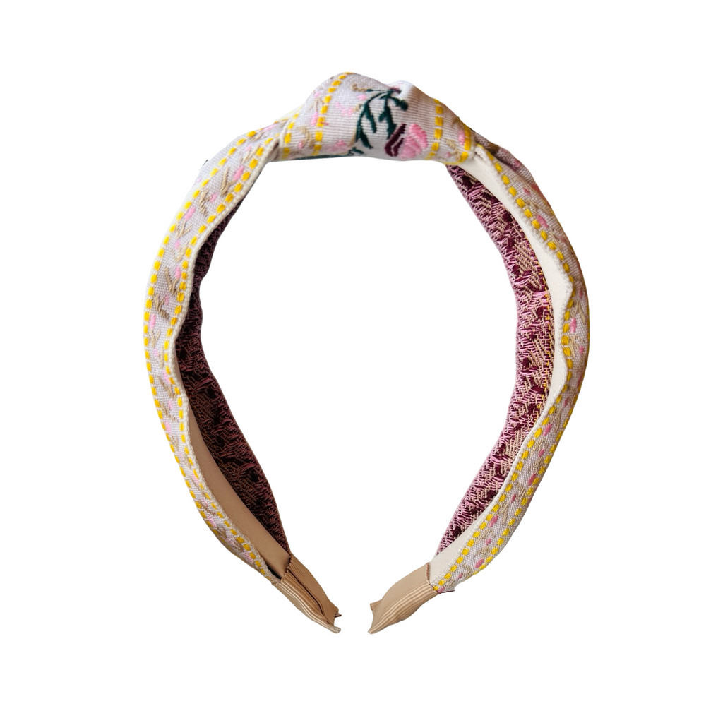 front view of a cream headband with a flower design in pink,maroon and yellow with some green foliage.