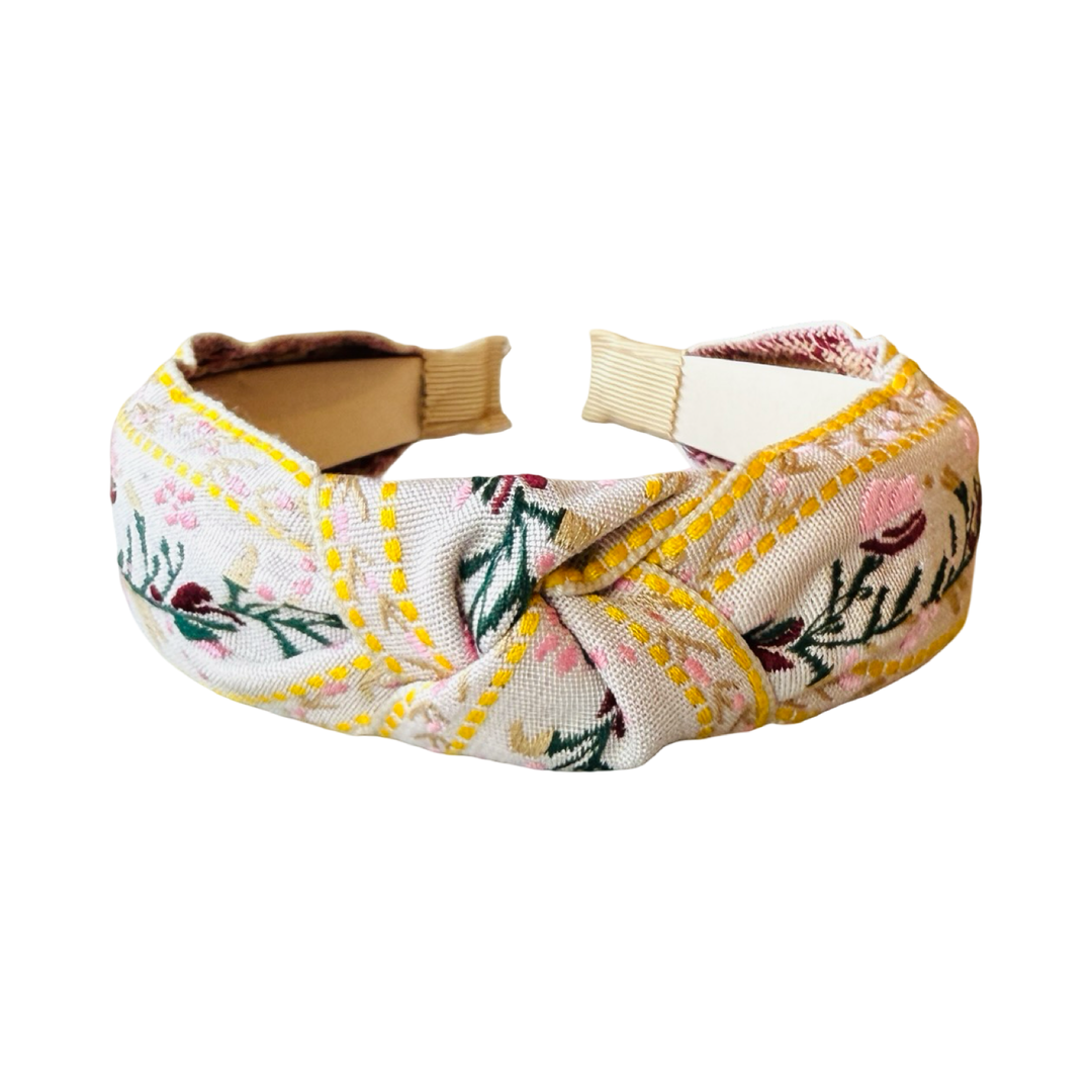 cream headband with a flower design in pink,maroon and yellow with some green foliage.