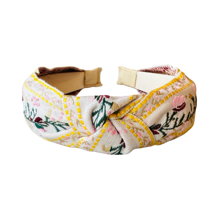 Cream headband with a flower design in pink, maroon and yellow with some green foliage.