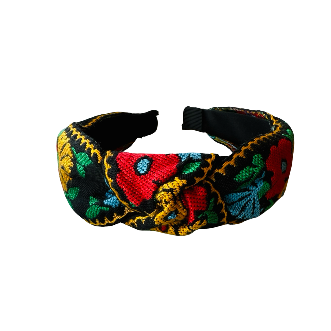 Top view of a black headband with a bold colorful floral design in yellow, red, blue and green.